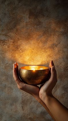 A pair of hands gently cradling a singing Tibetan bowl, illuminated by soft candlelight. Natural stone colors and a serene beige-brown background. No text, pure photo realism. Mantra