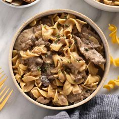 two bowls filled with pasta and meat on top of a marble table next to silverware