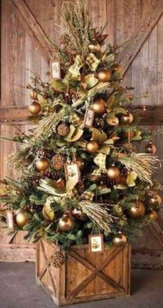 a christmas tree with gold ornaments and pine cones in a wooden box on the floor