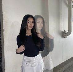 a woman standing in front of a mirror with her hair pulled back and wearing a skirt