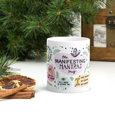 a coffee mug sitting on top of a table next to some cinnamon sticks and a pine tree