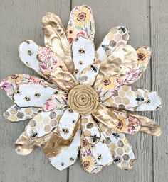 a flower made out of fabric and gold foil on top of a wooden surface with bees