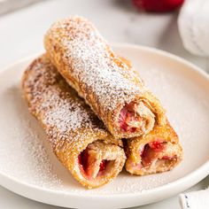 two pastries on a plate with powdered sugar and strawberries in the background