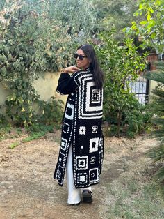 a woman standing in the dirt wearing a black and white cardigan sweater with geometric design