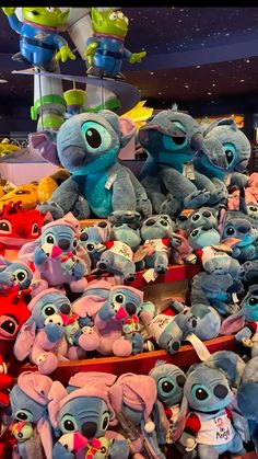 many stuffed animals are stacked on top of each other in a store display case with lights above them