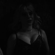 a woman wearing a bra in the dark with her hand on her hip and looking down