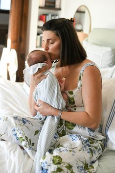 a woman holding a baby in her arms while sitting on a bed with white sheets