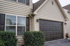 a house with two garages and bushes in front of the door, on a cloudy day