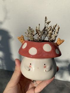 a hand holding a ceramic mushroom planter with flowers in it's top,