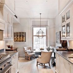 an elegant kitchen with white cabinets and wood flooring is pictured in this image, there are two chairs at the center of the room