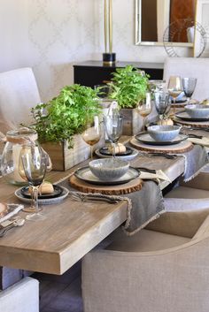 a dining room table set with place settings and plates, silverware and plants in vases