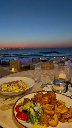 two plates of food sit on a table overlooking the ocean at dusk with candles lit