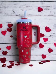 a red travel mug with hearts scattered around it on a white wooden background, surrounded by confetti