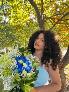 a woman holding a blue and white bouquet in her hands while standing next to a tree