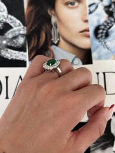 a woman's hand holding an emerald and diamond ring in front of a magazine