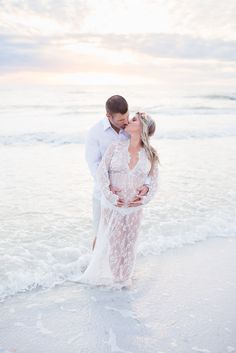 a man and woman kissing on the beach in front of the ocean at sunset during their engagement session