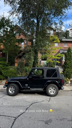 a black jeep parked on the side of a road in front of some trees and houses