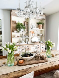 a wooden table topped with lots of vases filled with flowers next to an old dresser