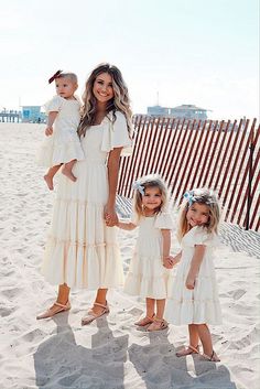 three girls in white dresses standing on the beach with their mother and two younger sister