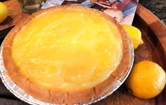 a pie sitting on top of a wooden table next to lemons and a magazine