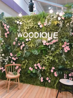 a green wall with pink flowers and greenery on it, surrounded by two chairs