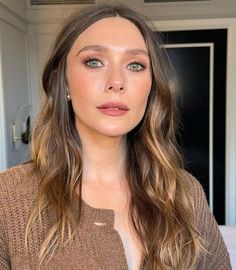 a woman with long hair and blue eyes wearing a brown sweater looking at the camera