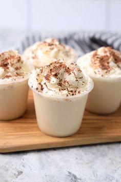 four dessert cups with whipped cream and chocolate sprinkles on a wooden tray