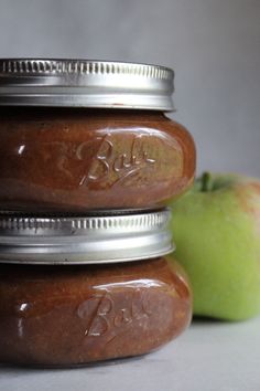 three jars filled with peanut butter next to an apple