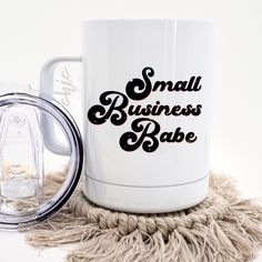 a white coffee mug sitting on top of a table next to a glass cup with the words small business babe printed on it