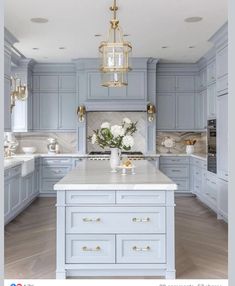 a large kitchen with blue cabinets and white counter tops, gold accents on the chandelier