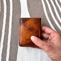 a hand holding a brown leather wallet on top of a striped cloth covered surface with white and black stripes