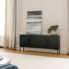 a living room with a large painting on the wall next to a black and white cabinet