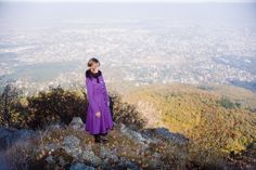 a woman in a purple dress standing on top of a mountain