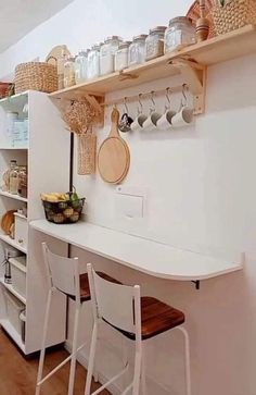 a kitchen with white walls and wooden flooring next to shelves filled with jars, pans and utensils