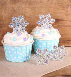 two cupcakes with frosting and snowflakes on them sitting next to each other