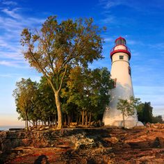 a white and red light house sitting on top of a rocky cliff next to trees