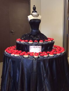 a black and red wedding dress cake with cupcakes on the bottom tier, sitting on a table