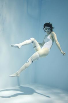 a woman floating in the water wearing a white body suit and goggles with her legs spread out