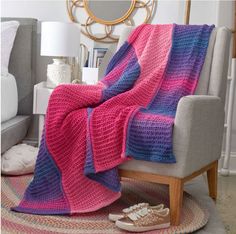 a pink and blue crocheted blanket sitting on top of a chair next to a lamp