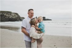 a man and woman holding a baby on the beach