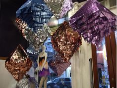 several different colored lights hanging from the ceiling in front of a store window with mannequins on display