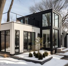 a modern house with black and white sidings in the wintertime, surrounded by snow