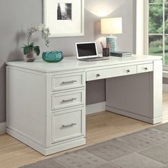 a white desk with a laptop computer on top of it next to a lamp and window