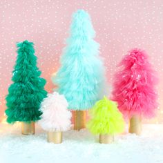 three small christmas trees in gold vases with pink, green and blue feathers on them