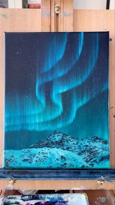 an easel with a painting on it and the aurora lights in the sky above