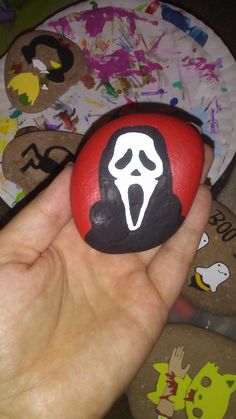 a hand holding a painted rock with a screamy face on it in front of other rocks