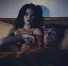 a woman laying in bed next to a man with dark hair and makeup on her face