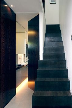 black stairs leading up to the kitchen and dining room in this modern home with white tile flooring