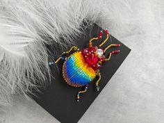 a colorful beaded bug sitting on top of a black piece of paper next to white feathers