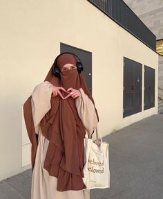 a woman wearing head covering and holding a bag standing in front of a building with doors